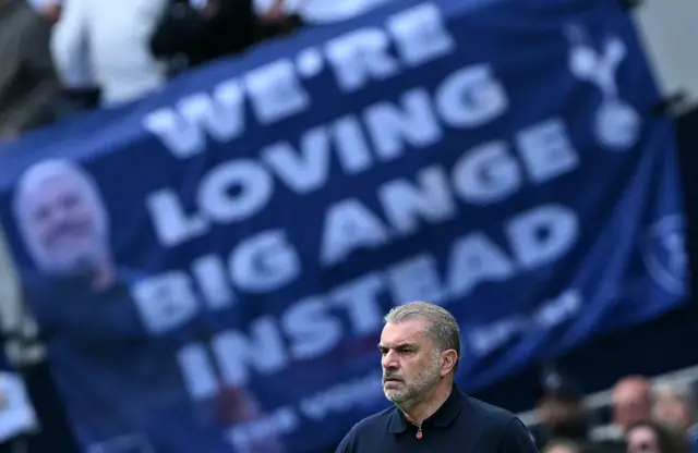 Ange Postecoglou in front of a banner saying 'We're loving Big Ange instead'