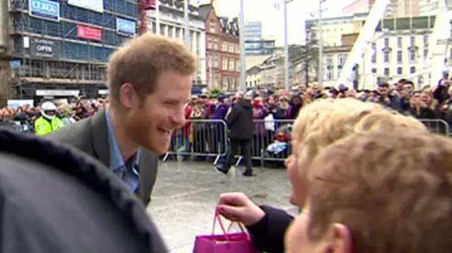 Prince Harry with a big smile talking to someone in a large crown in Nottingham
