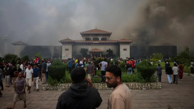 Demonstrators gather as smoke rises from the Parliament complex.