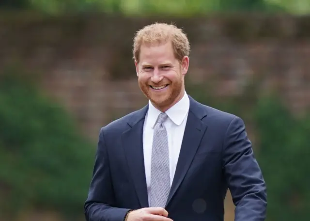 Prince Harry smiling while wearing a blue suit and a silver tie