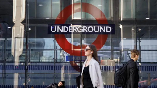 London Underground sign on side of building while woman walks past