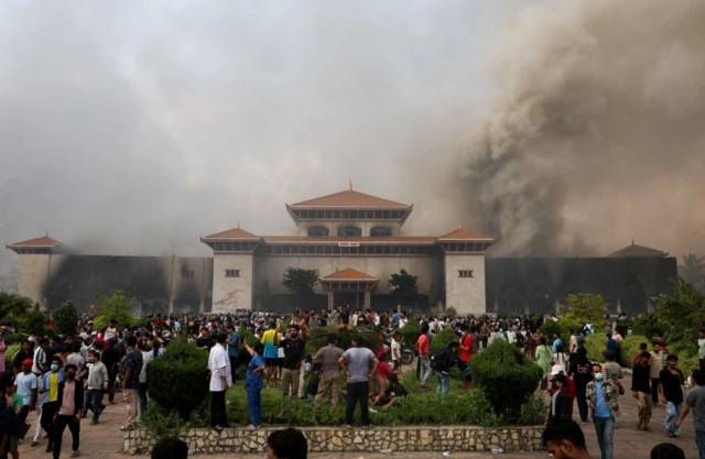Demonstrators gather as smoke rises from the Parliament complex following fire
