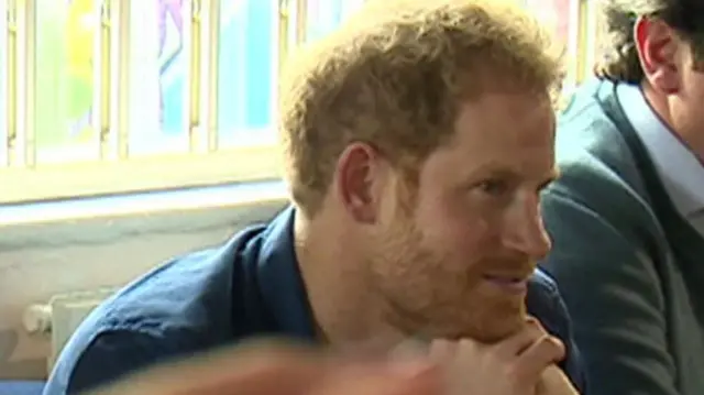 Prince Harry with his hands under his chin and a phone out of focus at the front of the image