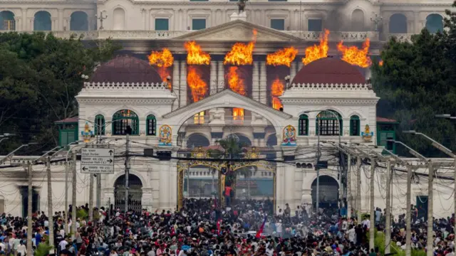 Parliament building in Nepal on fire, crowds stood outside.