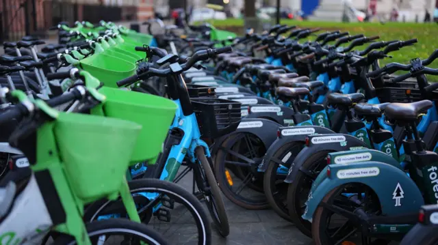 Rows of green Lime bikes and blue Forest bikes stacked against each other
