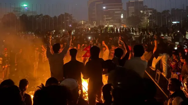 Hundreds of protestors chant and dance around fires in the parliament grounds, waving the Nepalese flag as smoke rises into the air.