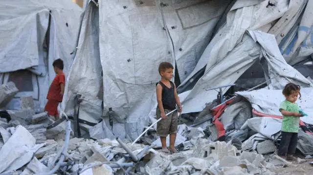 Children standing in a tent that has been ruined surveying the damage