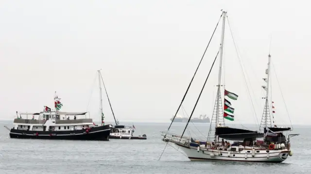 Two boats in the water with multiple Palestinian flags on their masts