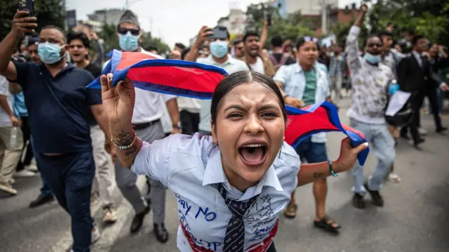 A young female protester in Nepal, with the Nepali flag draped on her back, walks at the front of an anti corruption protest
