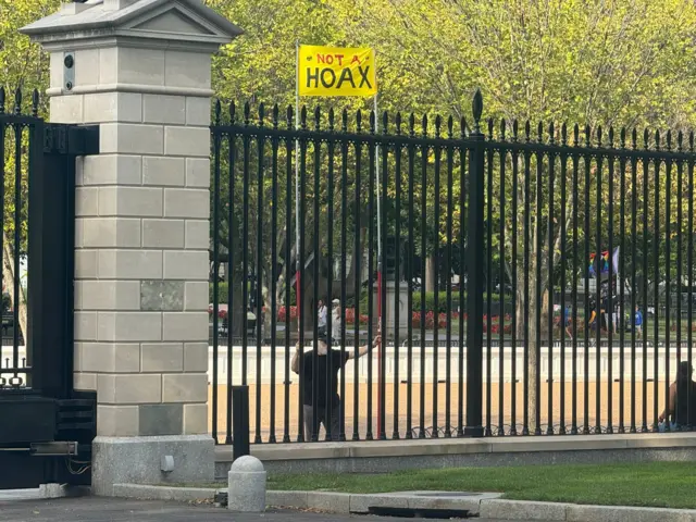 A man holding a yellow 'not a hoax' sign near the White House