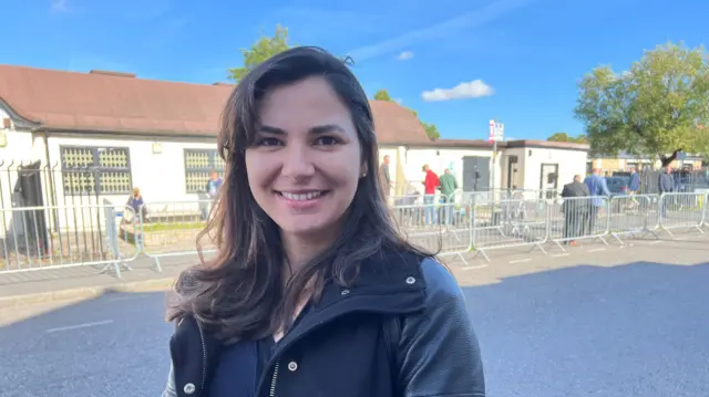 Diana De Faria, in a black leather jacket standing in front of silver barriers