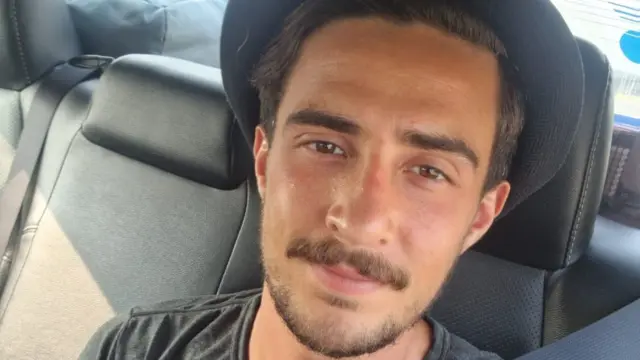 Joseph Glass looks at the camera with a seatbelt over his shoulder as he sits at the back of a car