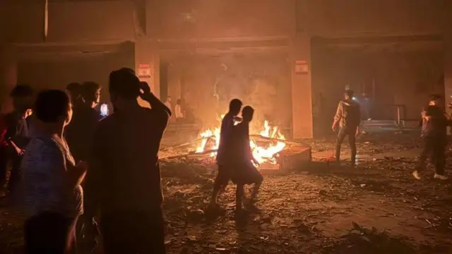 Protestors congregate outside the Parliament building, where a fire burns.
