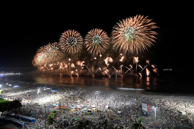Yellow fireworks explode on Copacabana Beach during celebrations in Rio de Janeiro, Brazil, with massive crowds gathered on the beach
