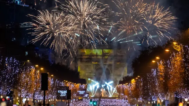 Revelers look at a light and fireworks show displayed on the Arc de Triomphe to celebrate the New Year 2026