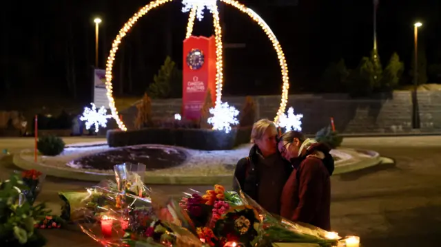A couple embrace near floral tributes