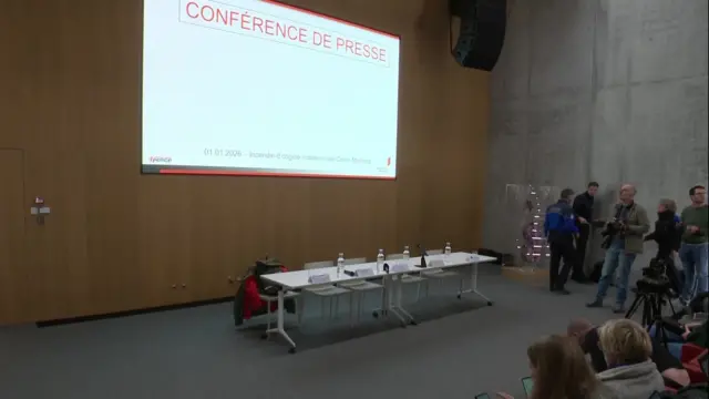 A screenshot of a table set up for a press conference and a projected screen above it