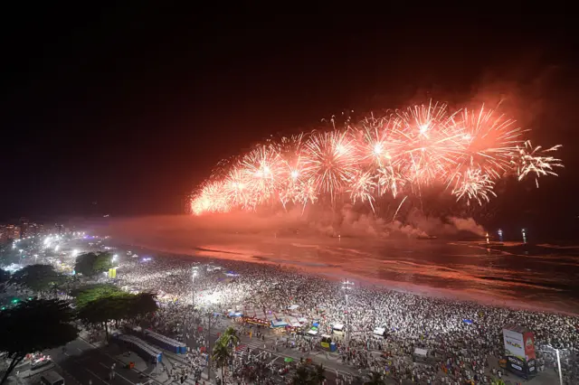 Orange fireworks explode on Copacabana Beach during celebrations in Rio de Janeiro, Brazil, with massive crowds gathered on the beach