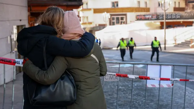 People embracing each other while looking at the bar, with police tape in the foreground