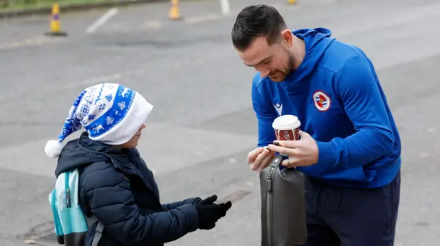 Jack Marriott of Reading handing something to a child wearing a winter hat in the car park after arriving at the match