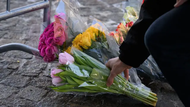 A woman's hand places a bunch of pale pink tulips wrapped in cellophane among other brightly-coloured flowers