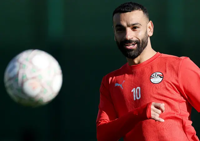 Mohamed Salah wearing a red top looks at a football