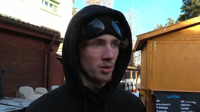 A young man speaks to the interviewer just off camera - he is wearing a black top with his hood up