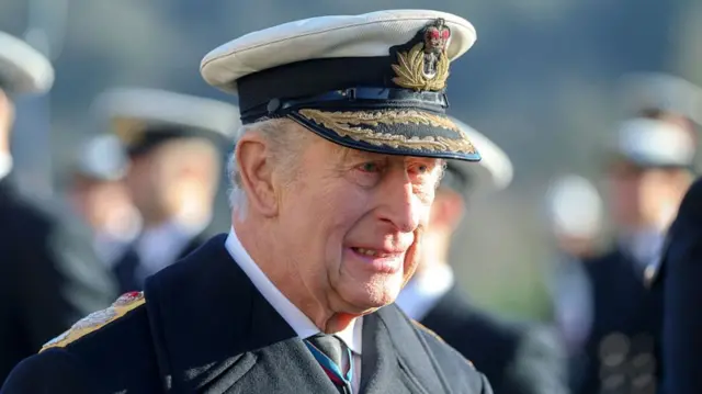 King Charles in dark uniform coat with shoulder marks and Navy officer cap