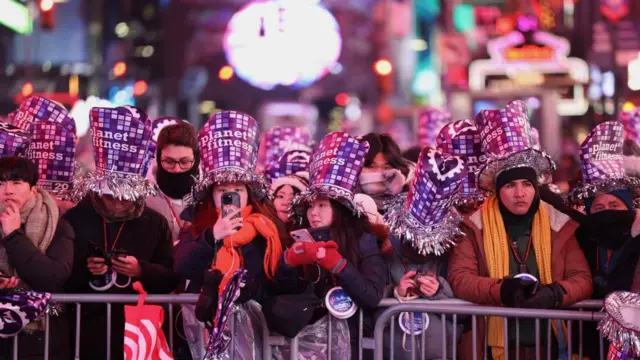 A large crowd of people wearing purple hats with the words "Planet Fitness" line up against a metal barricade in Times Square