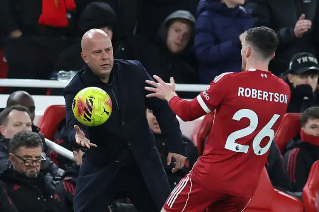 Liverpool's Dutch manager Arne Slot throws the ball to Liverpool's Scottish defender #26 Andrew Robertson