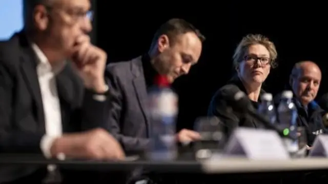 A row of four people at a press conference