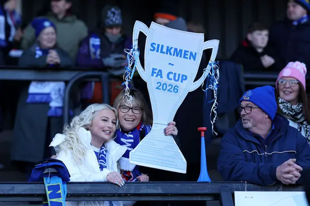 Fans holding cardboard cut-out of trophy with Silkmen FA Cup 2026 on it