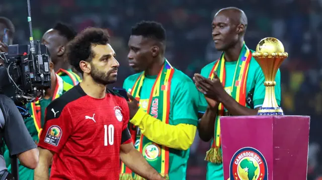 Mohamed Salah walks past the Africa Cup of Nations trophy