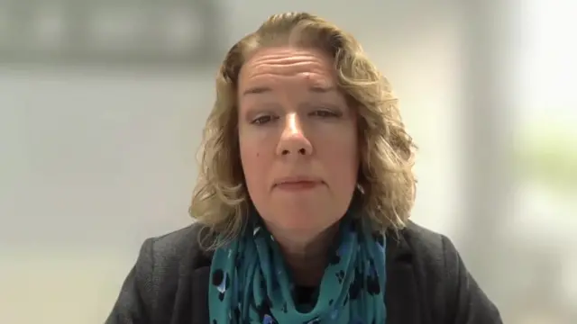 A woman speaking to her computer camera in a Zoom interview. She's wearing a black blazer and turquoise patterned scarf.