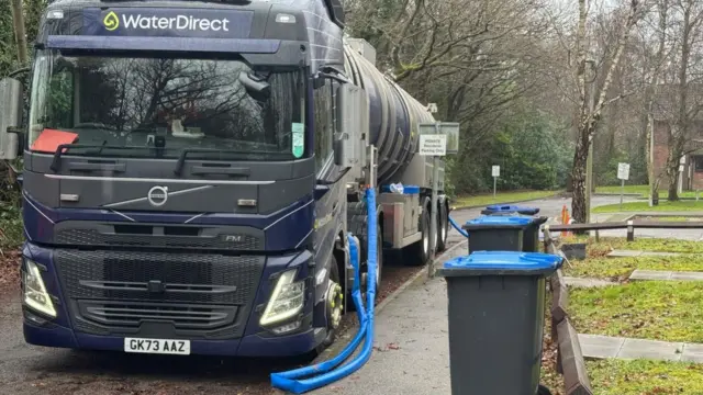 A tanker stands on hospital grounds. It has a Water Direct logo on the front and a blue pipe coming from the vehicle.