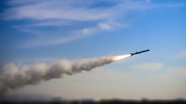 A missile being fired through the air with cloud behind it.