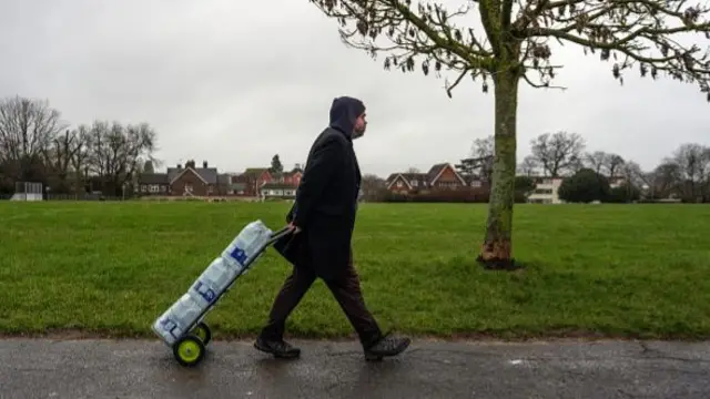 A man pulls a trolley of bottled water collected from an emergency water distribution point in East Grinstead.