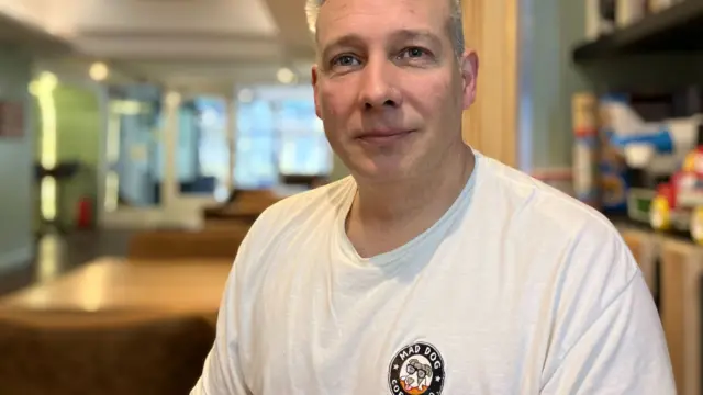 Russ Bullen wears a white sweat shirt and smiles into the camera.