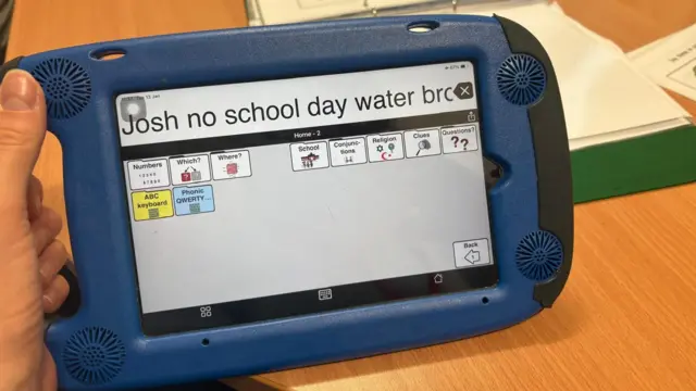 An iPad with the words 'Josh no school day water broken' on it. On the ipad screen are more buttons which create words in the type bar at the top