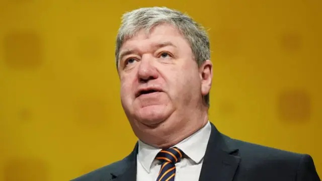 Alistair Carmichael in front of a yellow background.