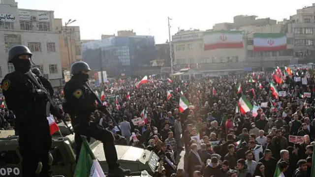 Two security personnel with guns survey a crowd