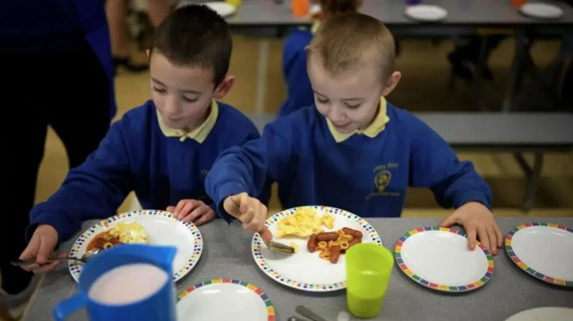 two boys in school uniform eat sausage and eggs breakfast in a school canteen