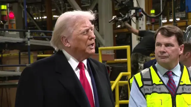Donald Trump in a suit and overcoat in a factory