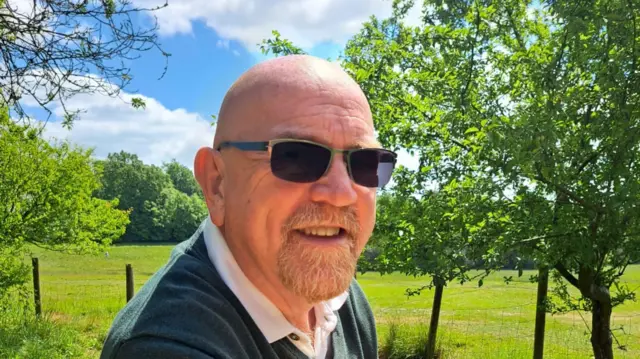 A man on a sunny day. He is wearing big, black sunglasses.