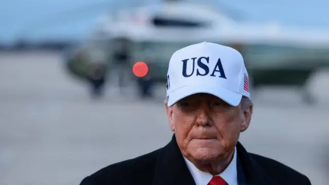 US President Donald Trump wearing a white cap with the letters 'USA' on the front.