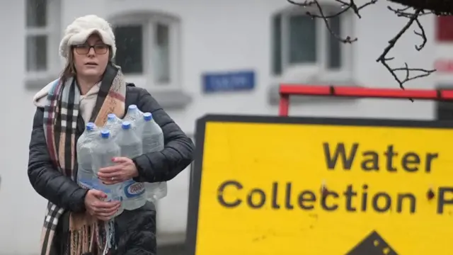A woman holds some plastic bottles in the rain.