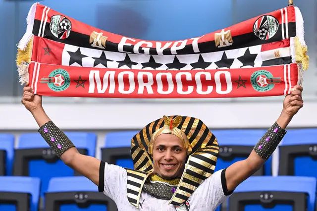 Egypt fan dressed as a Pharoah holds up a banner with 8 stars, Morocco and Egypt flags
