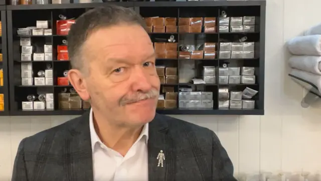Richard Dandy stands in his salon with products and towels behind him.