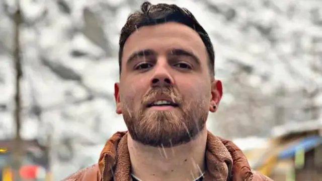Erfan Soltani, a young bearded man with short hair, wears a dark-orange winter jacket