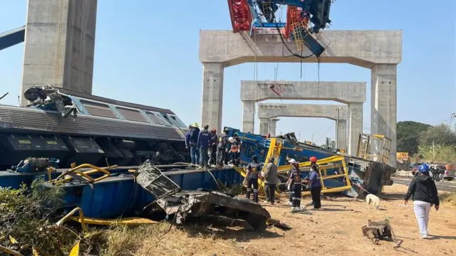 People with helmets standing near an overturned train carriage